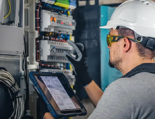 Electrician in safety gear inspecting electrical panel with tablet - Everyday Sparky Melbourne